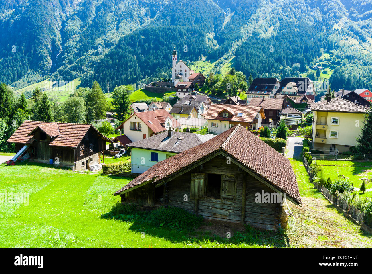 The village with a church is located in a high altitude landscape with mountains, green meadows and trees Stock Photo