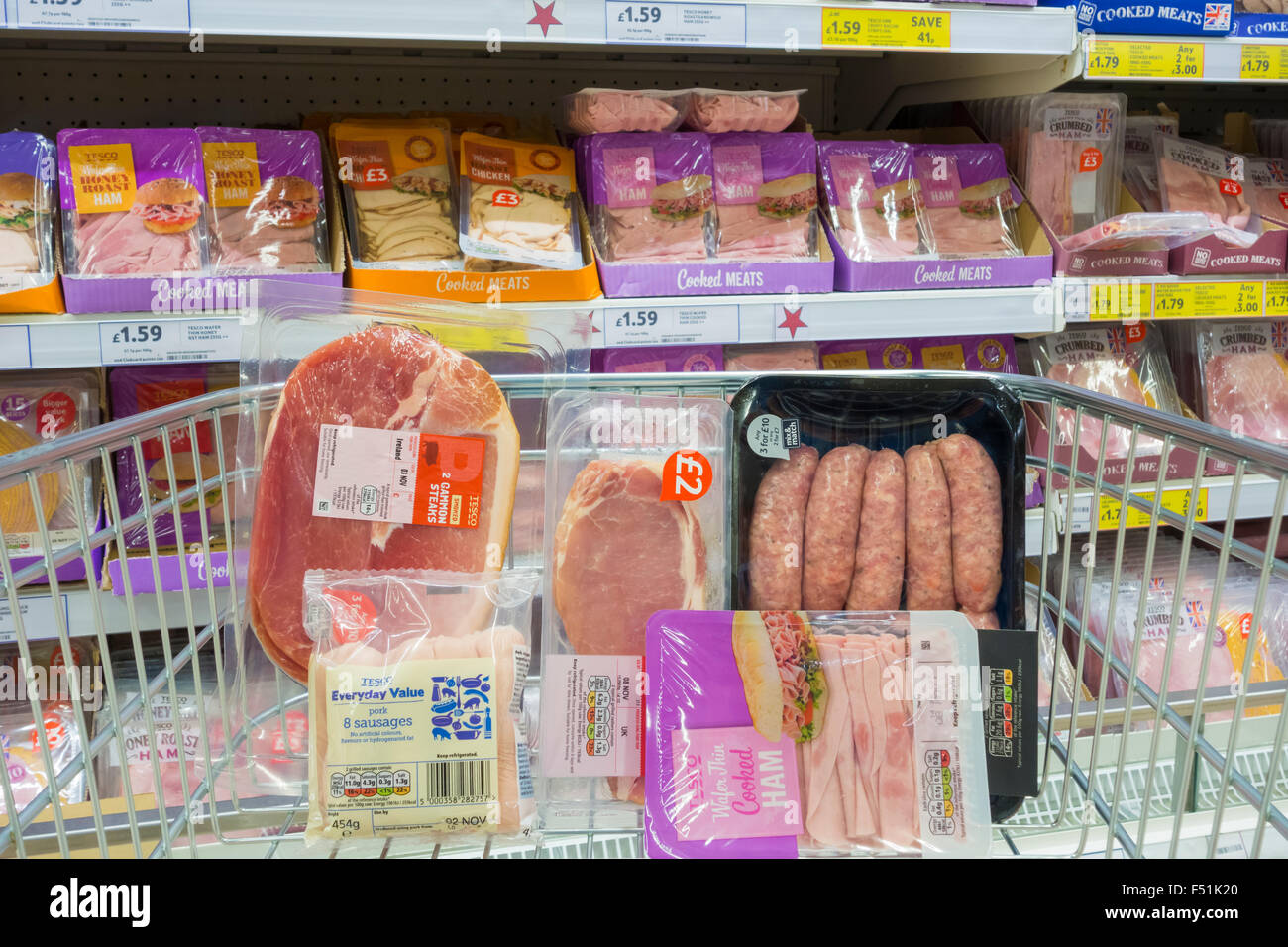 Processed meat (cooked ham), bacon, Gammon and sausages in plastic packaging in shopping trolley in Tesco supermarket. UK Stock Photo