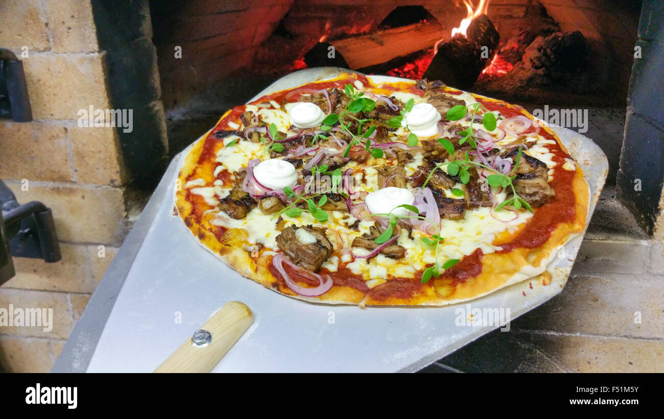 Taking a pulled pork pizza, with aioli, from a wooden warmed oven Stock Photo