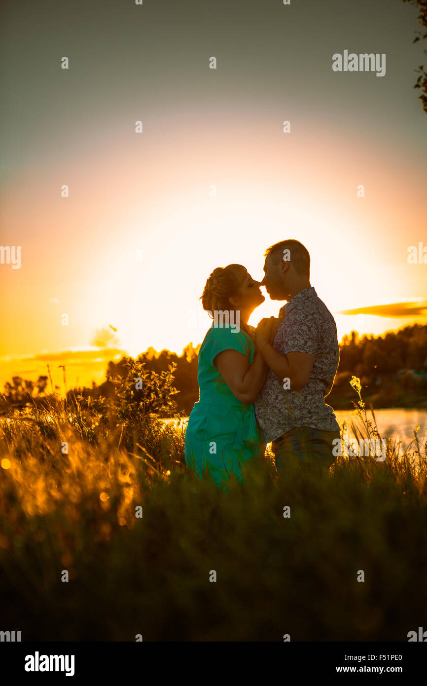 Romantic couple standing and kissing on background summer meadow sunset ...