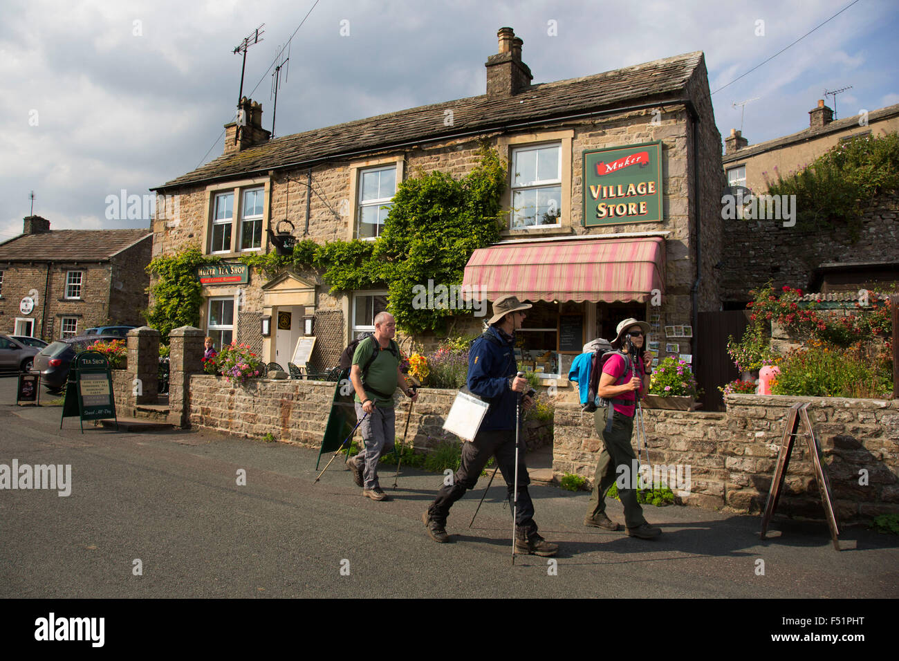 Hikers leave the village shop in Muker in Swaledale, which runs broadly from west to east. To the south and east of the ridge a number of smaller dales. Swaledale is a typical limestone Yorkshire dale, with its narrow valley-bottom road. Yorkshire, England, UK. Stock Photo
