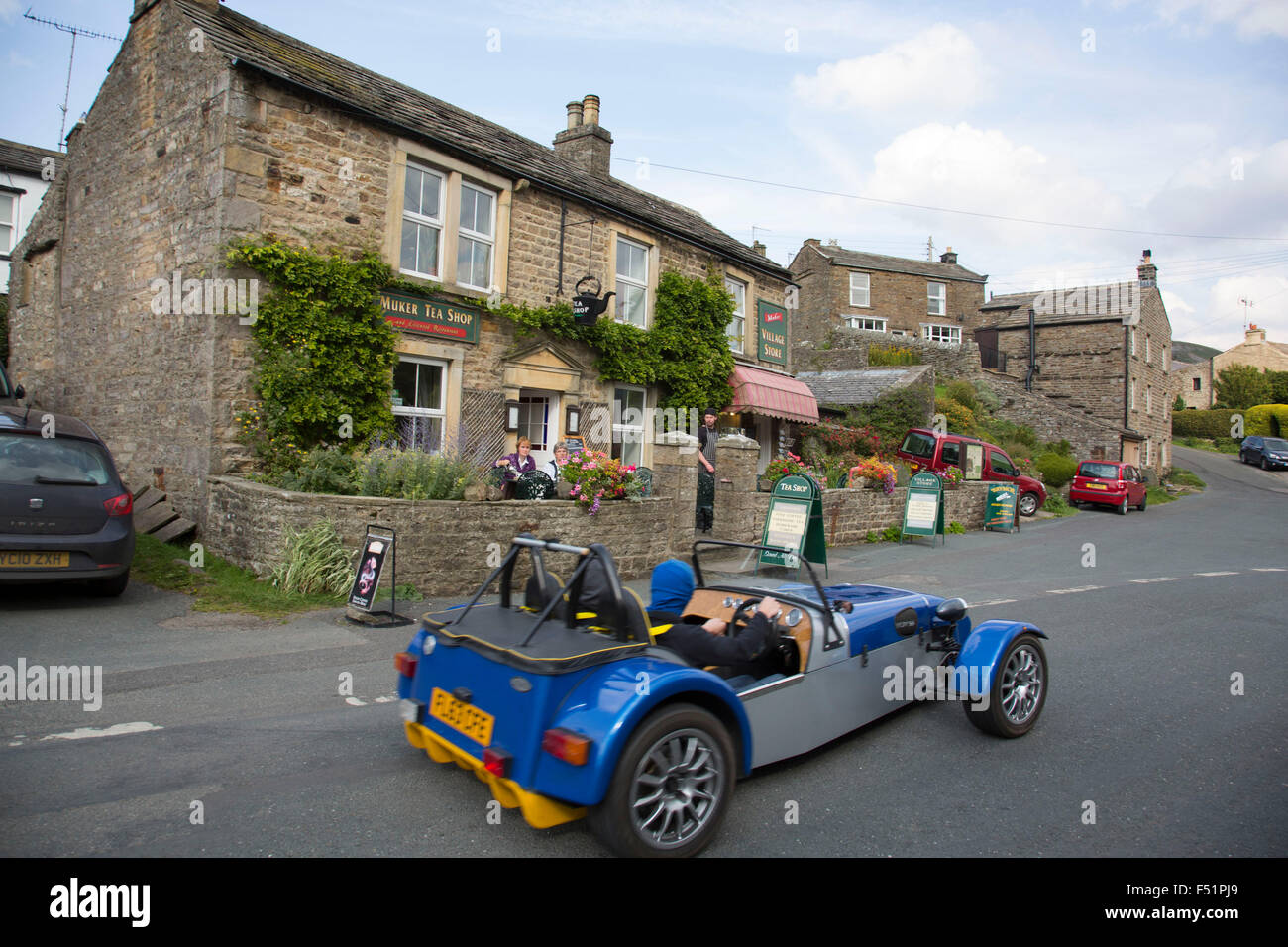 Kit car passes the village shop in Muker in Swaledale, which runs broadly from west to east. To the south and east of the ridge a number of smaller dales. Swaledale is a typical limestone Yorkshire dale, with its narrow valley-bottom road. Yorkshire, England, UK. Stock Photo