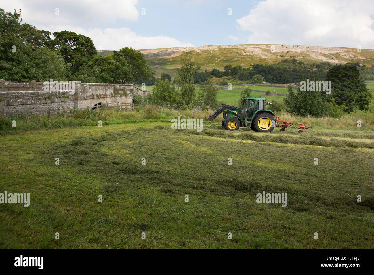 Farmer using a tractor to gather hay on the last day before rain is expected in his field in Reeth at Swaledale. Yorkshire, England, UK. This is a farming area where rural living and the countryside is at the centre of life in this county. Swaledale runs broadly from west to east. To the south and east of the ridge a number of smaller dales. Swaledale is a typical limestone Yorkshire dale, with its narrow valley-bottom road, green meadows and fellside fields, white sheep and dry stone walls on the glacier-formed valley sides, and darker moorland skyline. Stock Photo