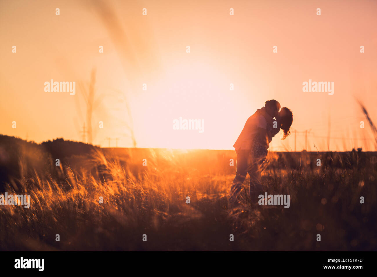 Romantic couple standing and kissing on background summer meadow sunset ...