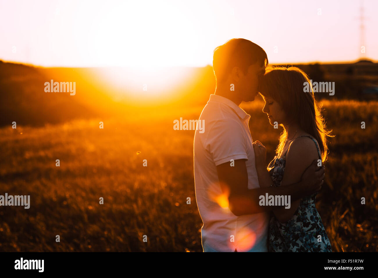 Romantic couple standing and kissing on background summer meadow sunset ...