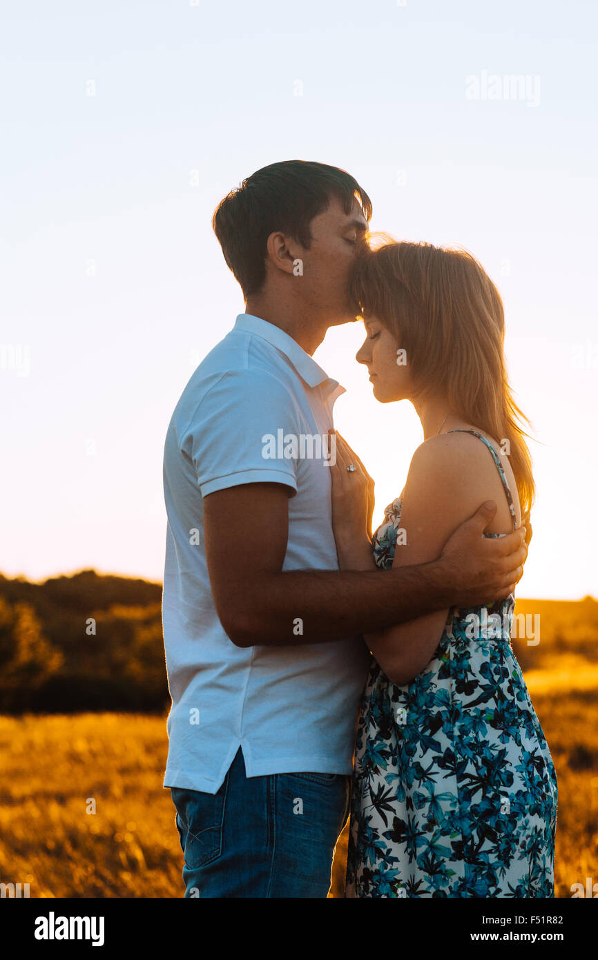 Romantic couple standing and kissing on background summer meadow sunset ...
