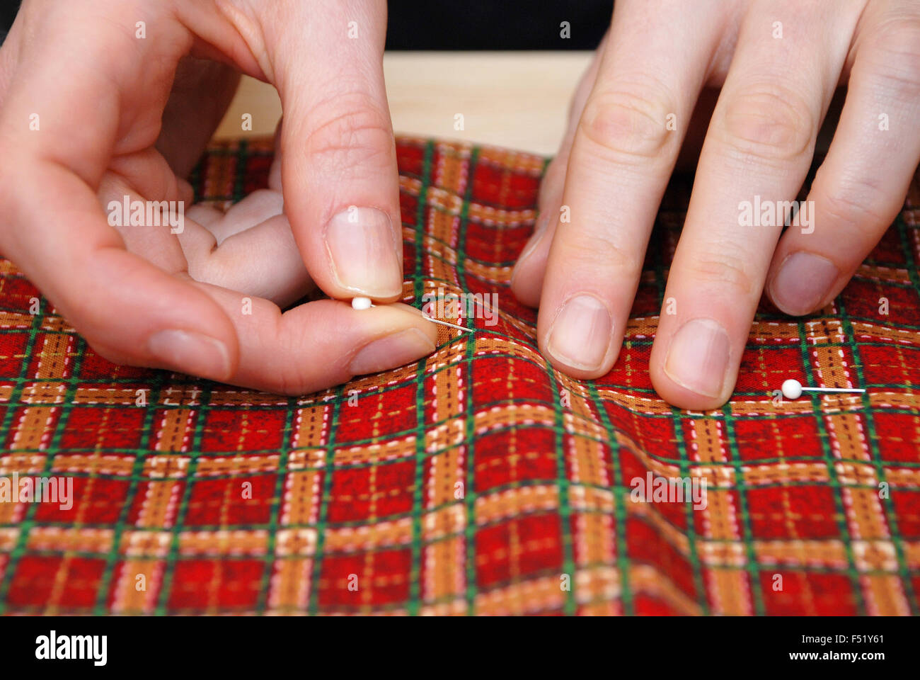 Closeup of two hands sticking pins into festive red plaid fabric Stock Photo