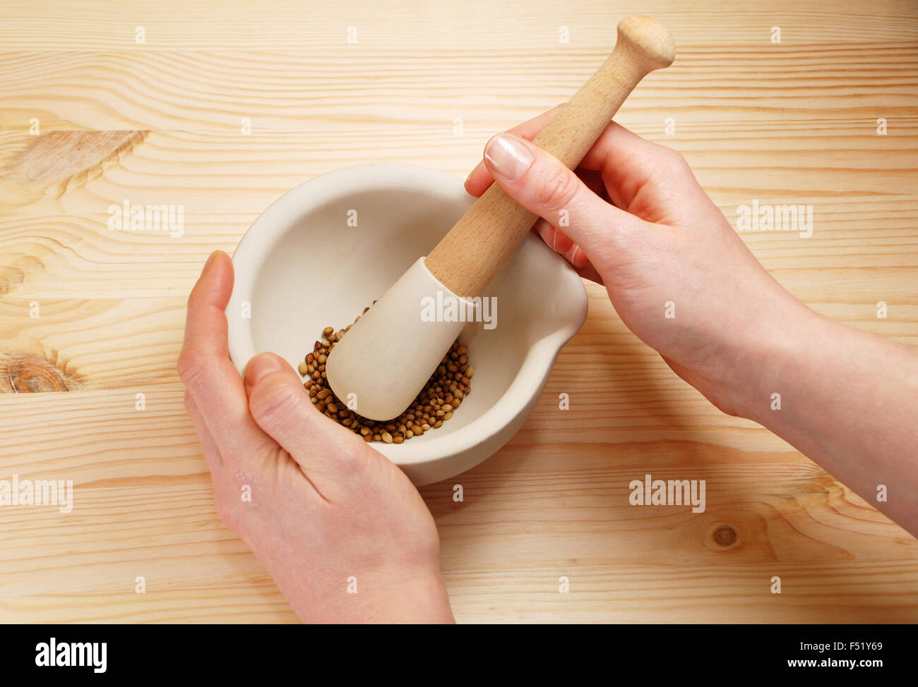 A woman uses a pestle and mortar on a wooden table to crush whole coriander seeds Stock Photo