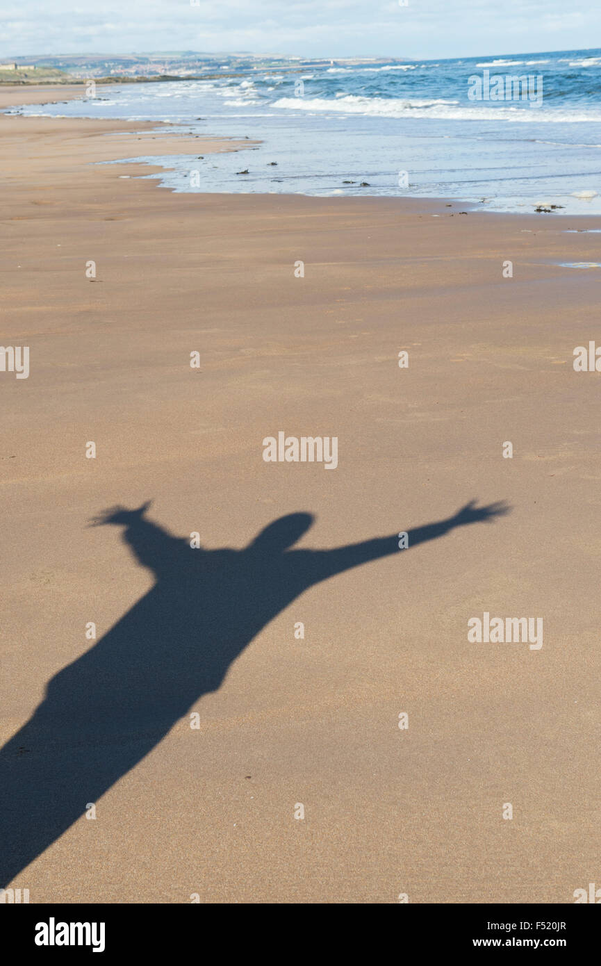 Shadow of a man with his arms in the air on a beach. UK Stock Photo