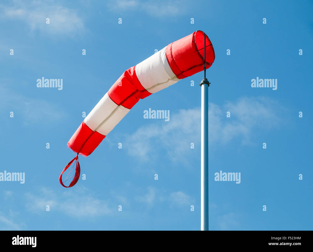 Frayed windsock in moderate wind against blue sky with few clouds Stock Photo
