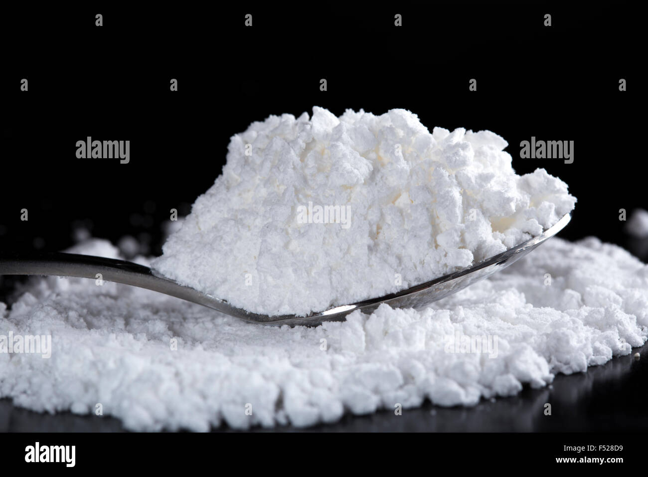 White powder in silver spoon over dark background Stock Photo