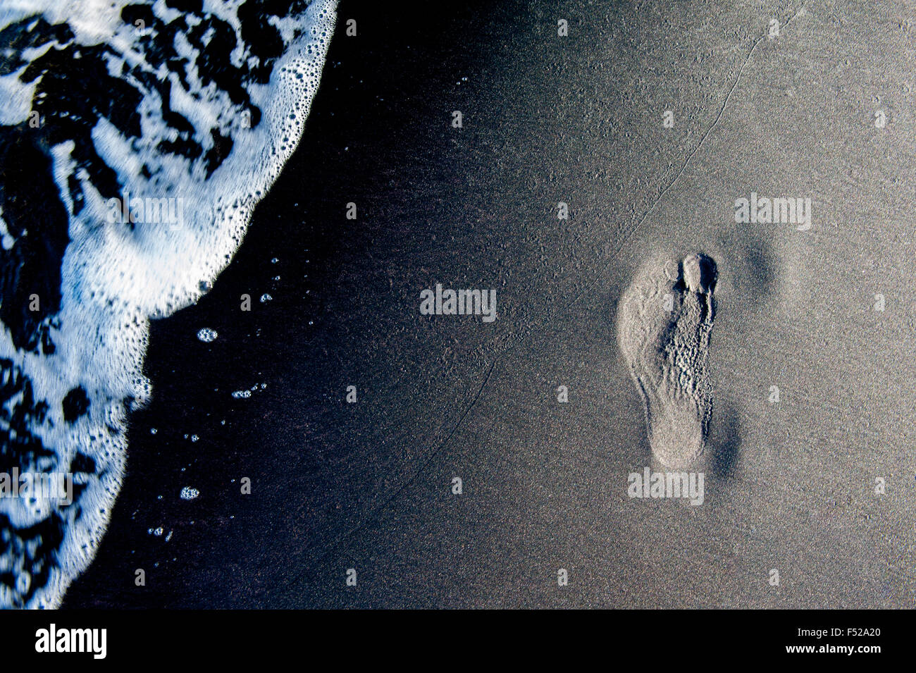 Human footprint placed on beach sand, water waves arriving Stock Photo