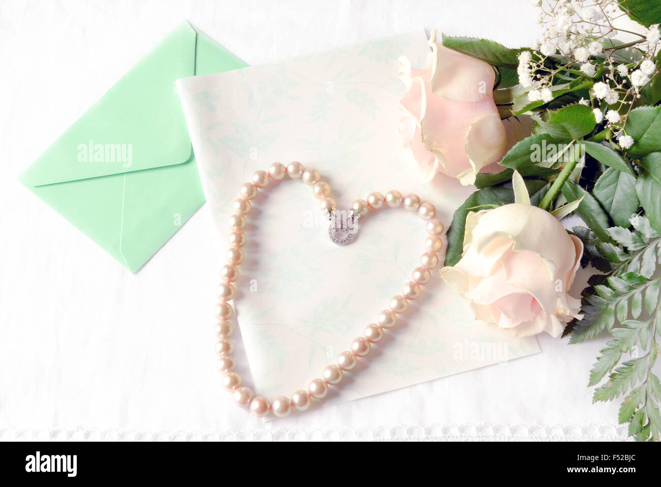 Pink roses lying on the table with an empty letter and a pink pearl necklace genuine of Japan. Stock Photo