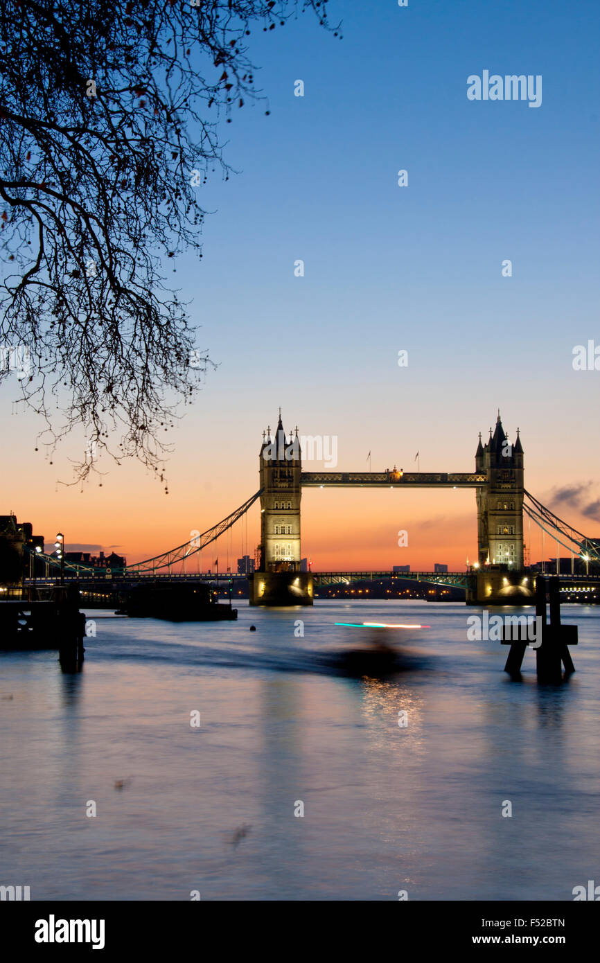 Tower Bridge and River Thames with boat passing through shot at dawn sunrise London England UK Stock Photo