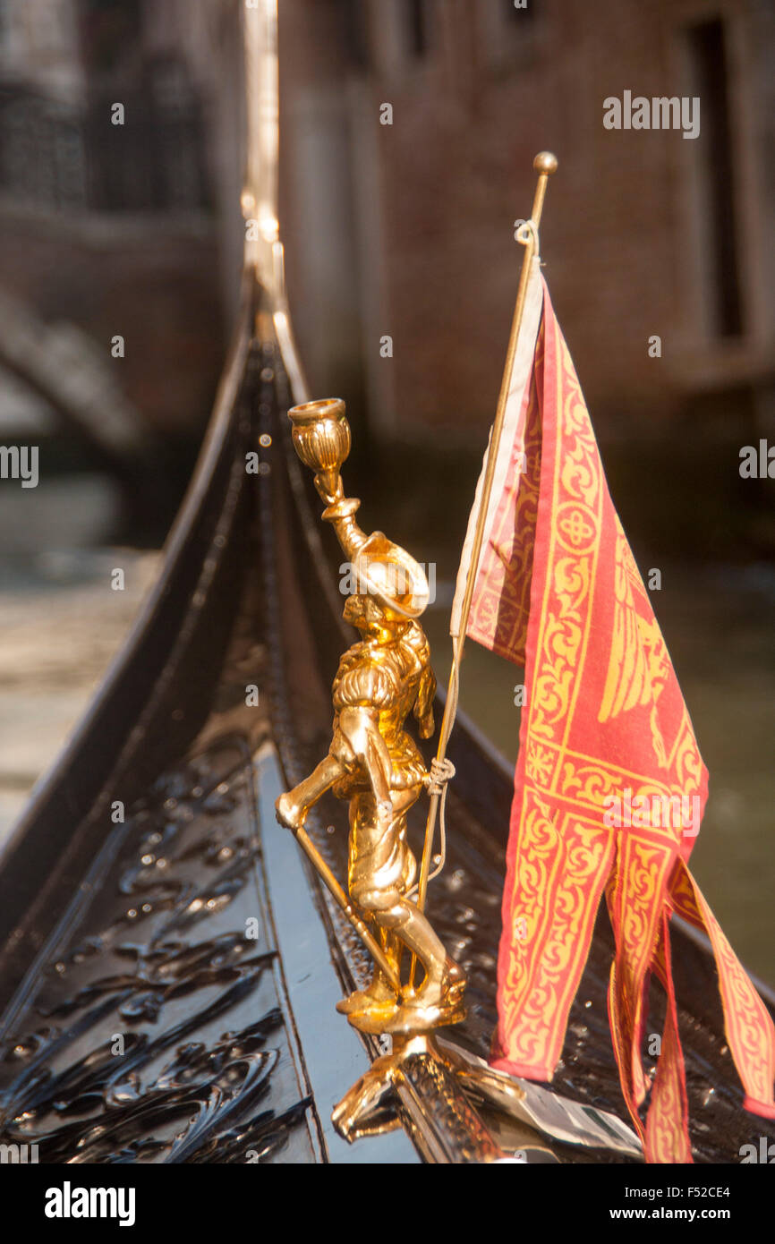 Figure and Venetian flag at front of gondola with canal and buildings ...