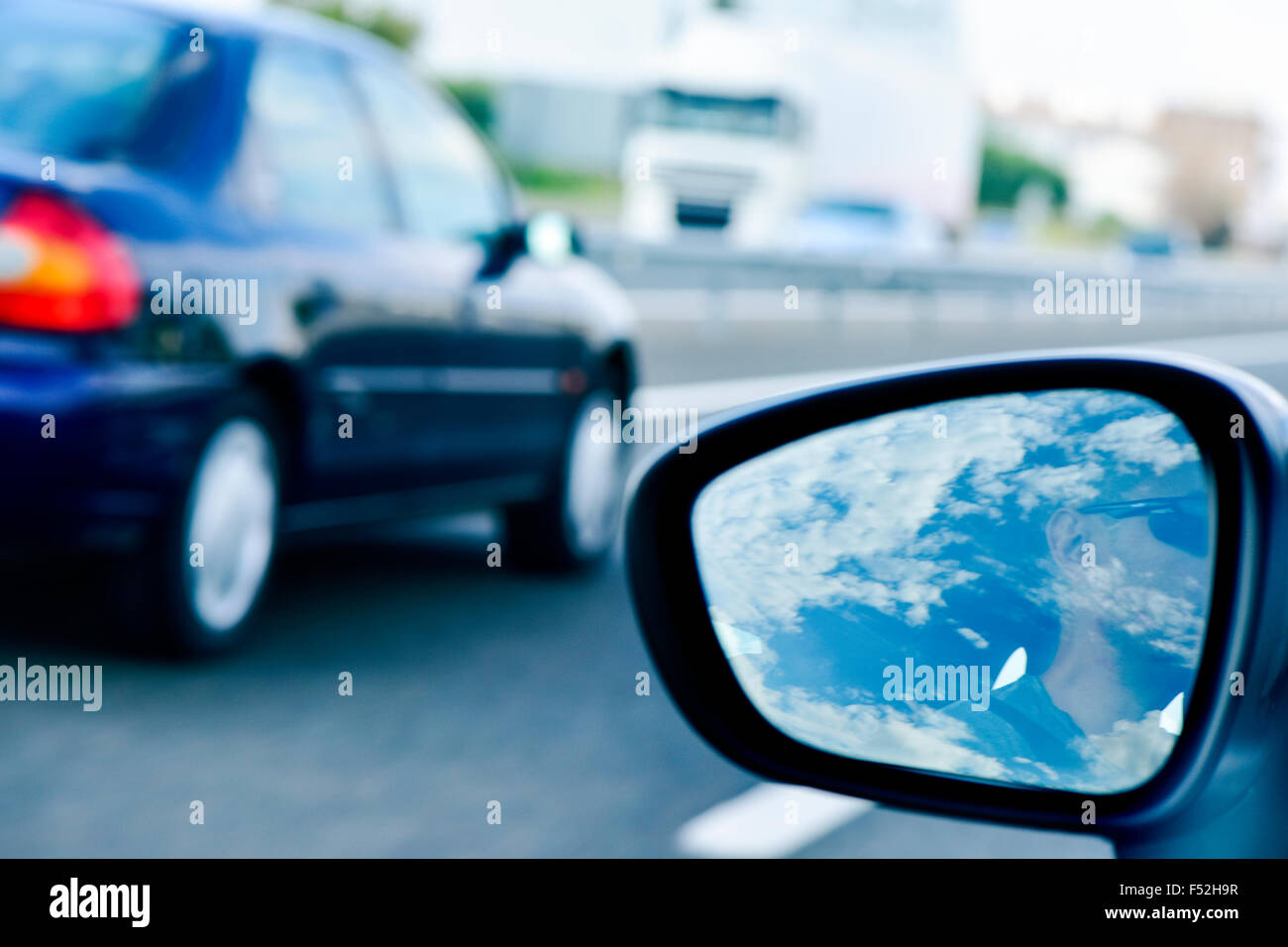 a young man, reflected in the wing mirror, driving a car in a road with several lanes, being passed by another car Stock Photo