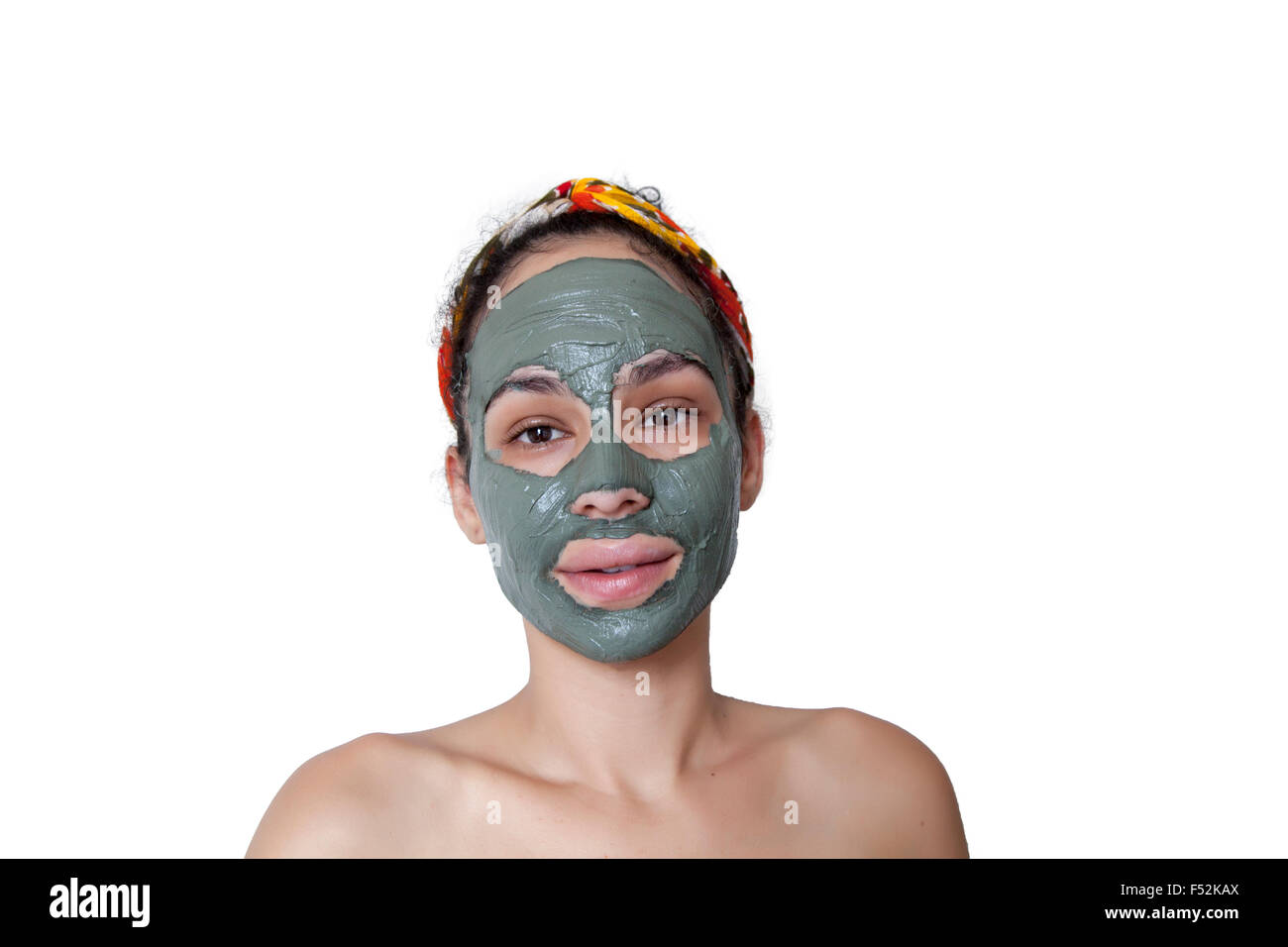 Beautiful young Brazilian model with green clay facial mask. Spa teen girl applying facial clay mask. Beauty treatments. Stock Photo