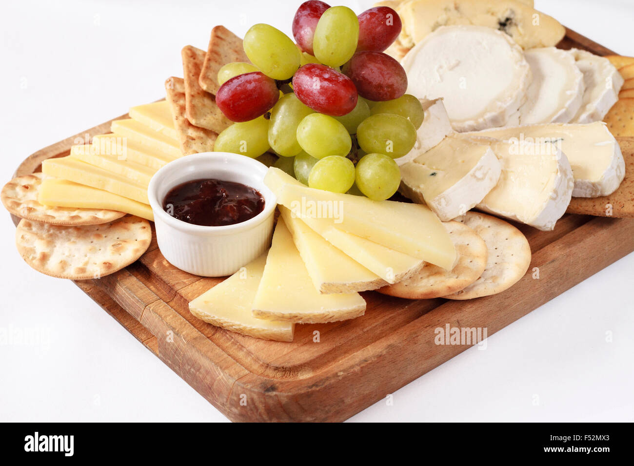 A platter of different cheese with grapes, biscuits, and raspberry jam