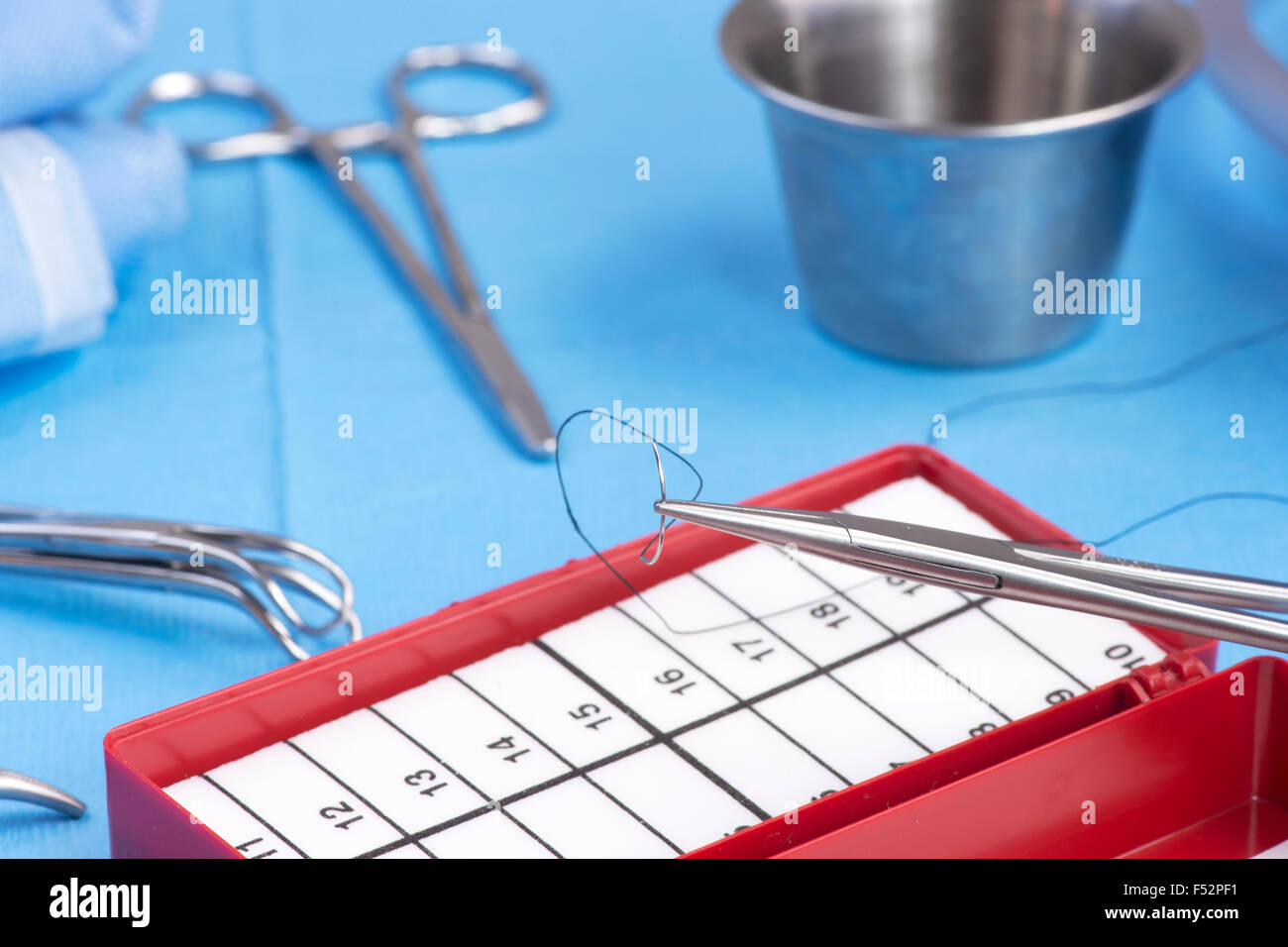 Needle holder with silk suture and needle counting box on blue sterile drape. Stock Photo