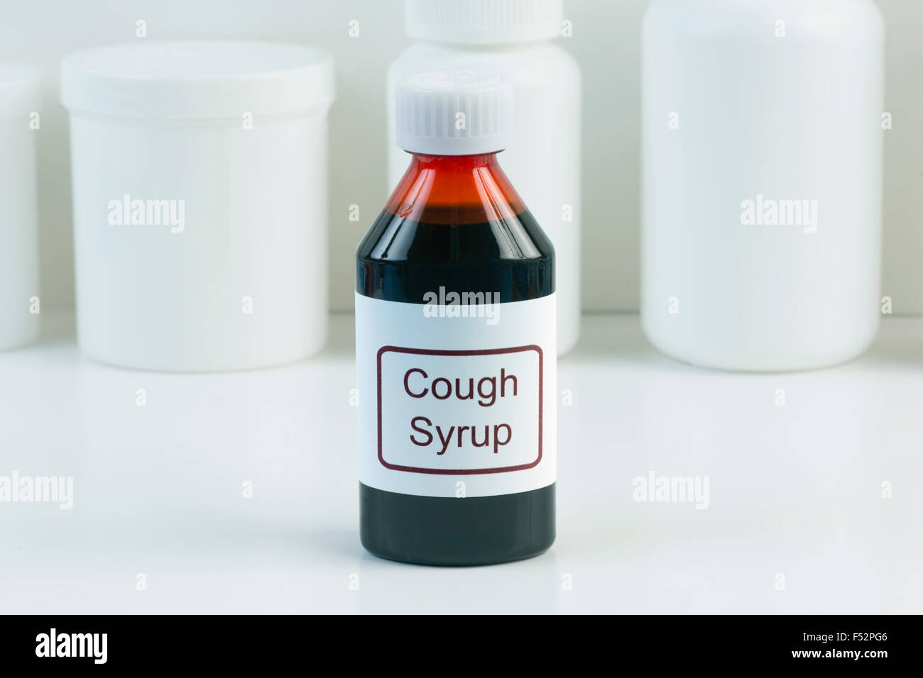 Cough medicine in amber bottle with white containers in background. Stock Photo