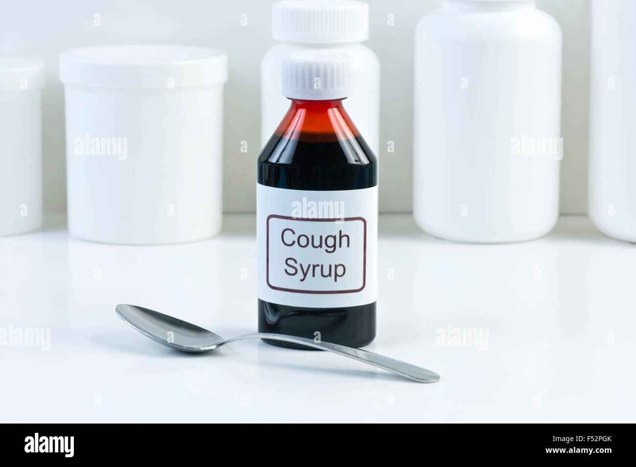 Cough medicine in amber bottle with spoon and white conatiners in background. Stock Photo