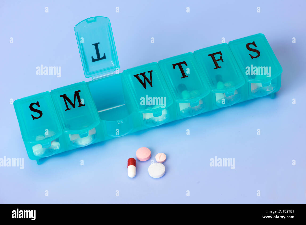 Daily pill dispenser with assorted pills on blue background. Stock Photo