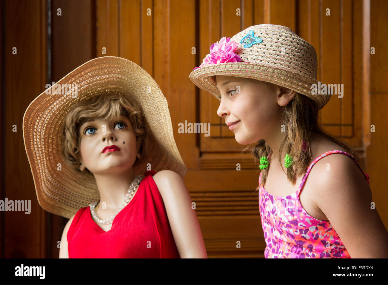 Young girl in a hat looking at a mannequin wearing a red dress and hat. Soft lighting and focus with warm vintage tones and look Stock Photo