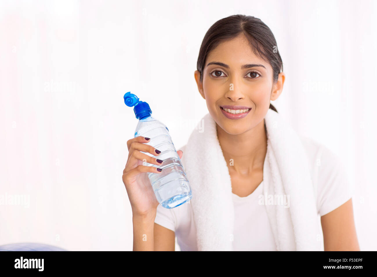 fit young Indian woman drinking water after exercising indoors Stock
