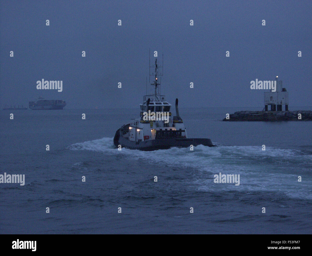 tug boat sailing out to assist containership Stock Photo