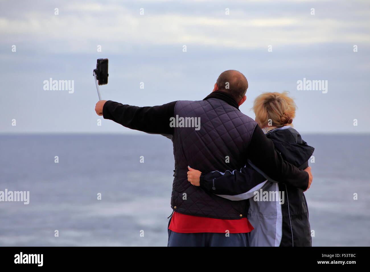 A man and a woman or couple taking a selfie picture with a smartphone on a selfie stick Stock Photo