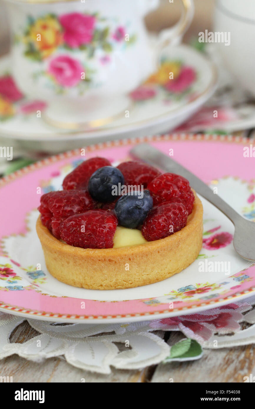 Delicious crunchy tartelette with custard, fresh raspberries and blueberries with cup of tea Stock Photo