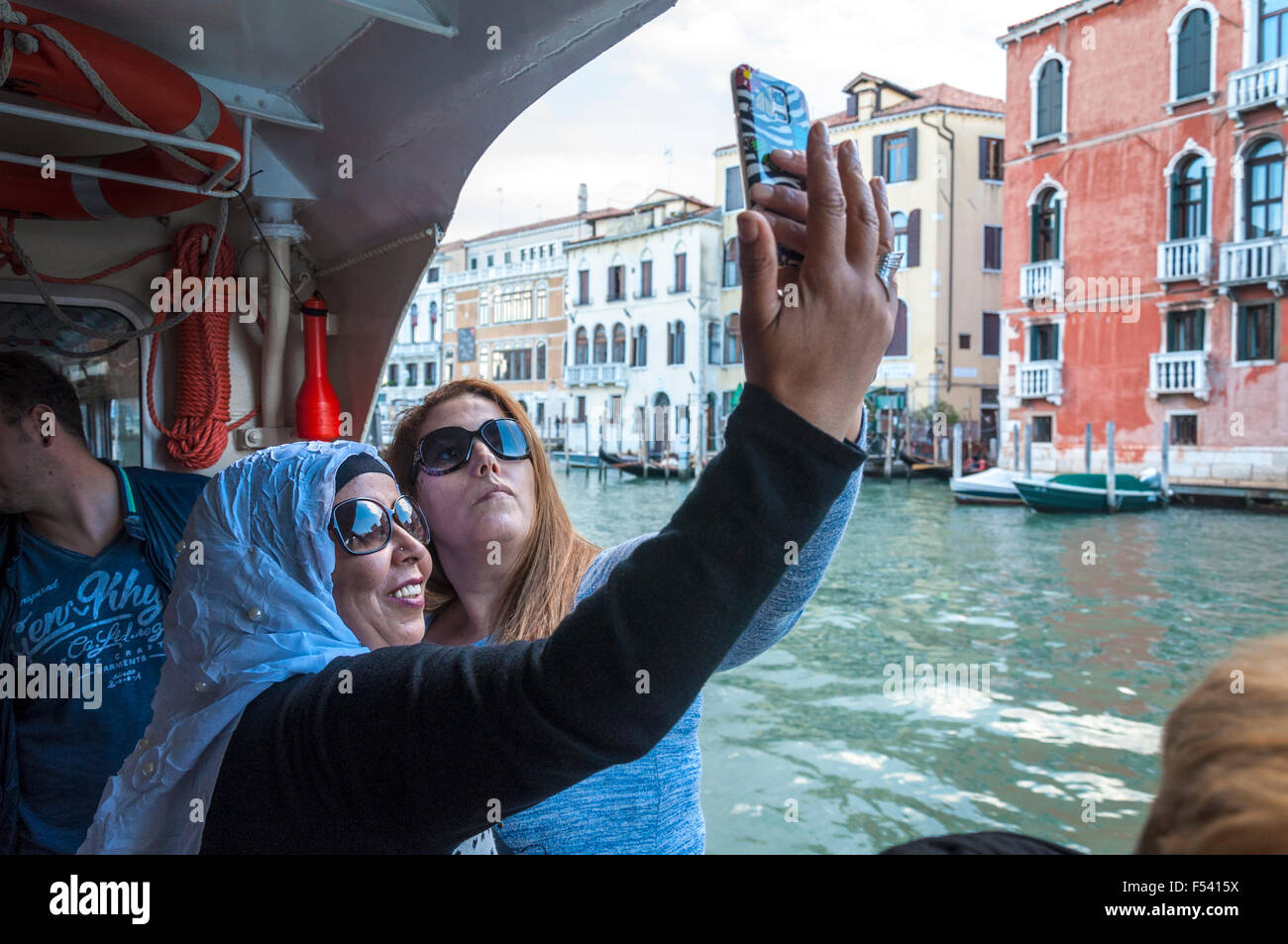 Two women take a selfie phone camera photo on a vaporetto on the grand Canal in Venice, Italy Stock Photo