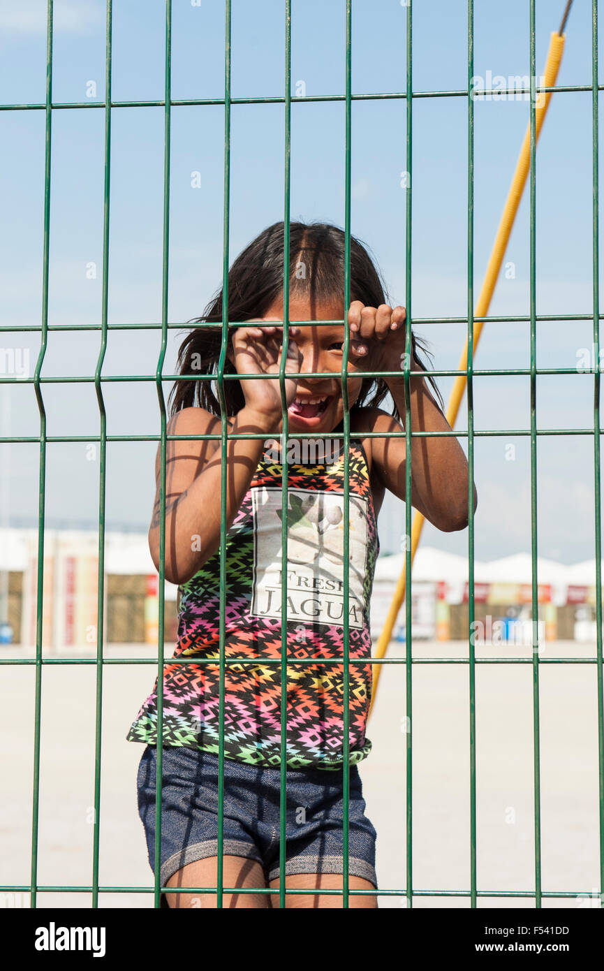Palmas, Brazil. 26th Oct, 2015. A Kayapo girl in western clothes but with traditional close-cropped strip of hair laughs through a wire mesh fence during the International Indigenous Games, in the city of Palmas, Tocantins State, Brazil. Credit:  Sue Cunningham Photographic/Alamy Live News Stock Photo