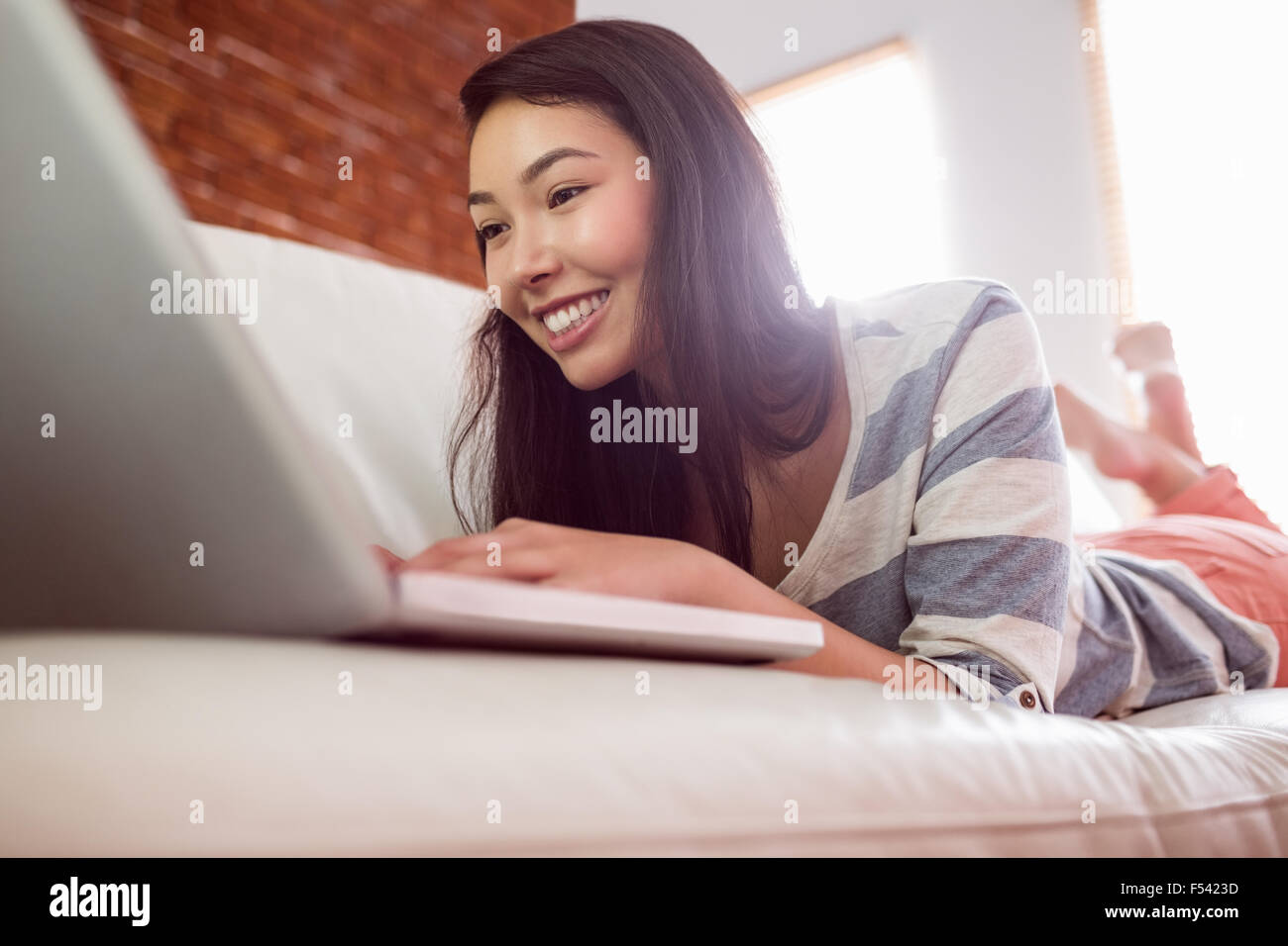 Smiling asian woman on couch using laptop Stock Photo - Alamy