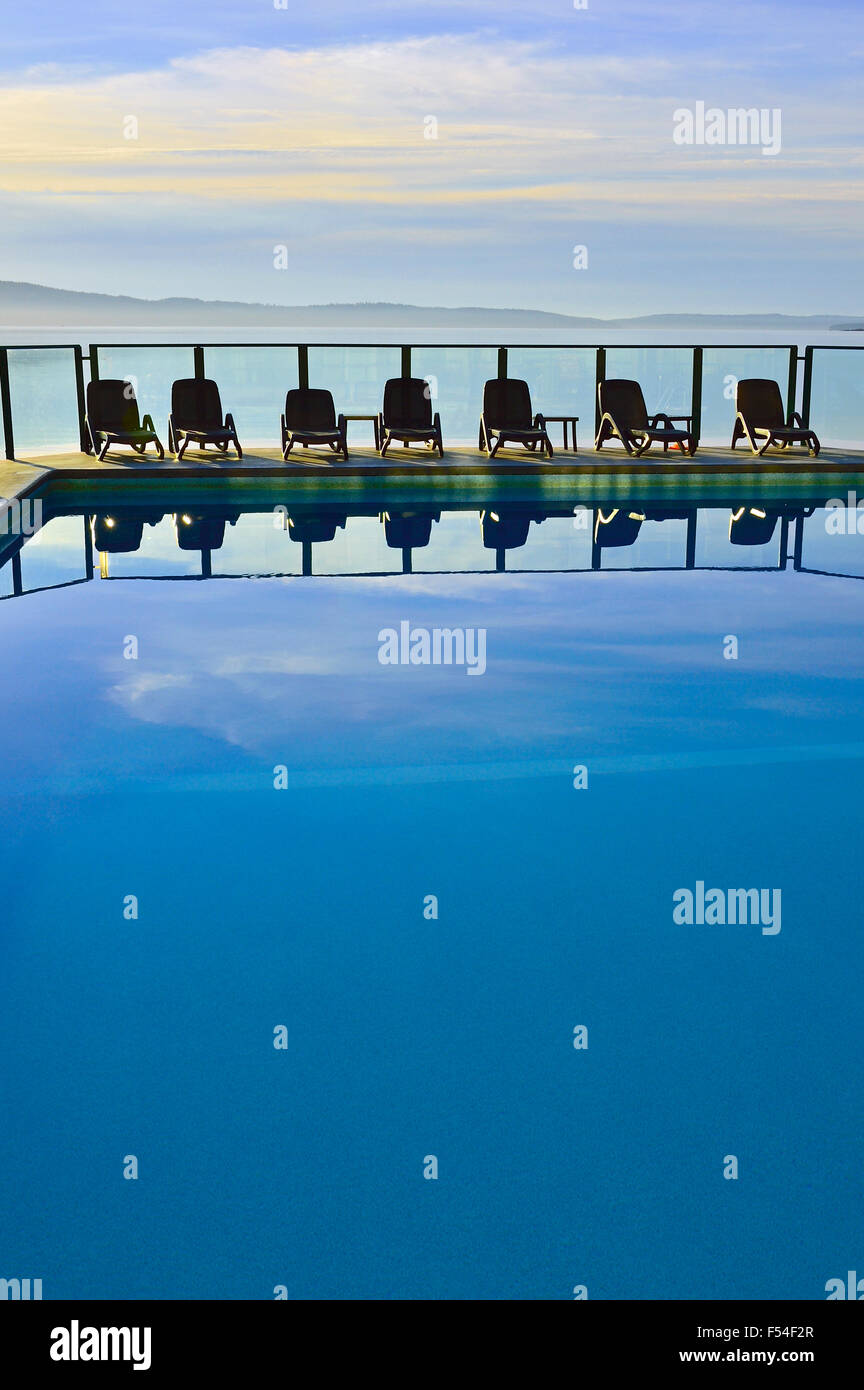 A vertical image of an outdoor swimming pool with a line of chairs Stock Photo