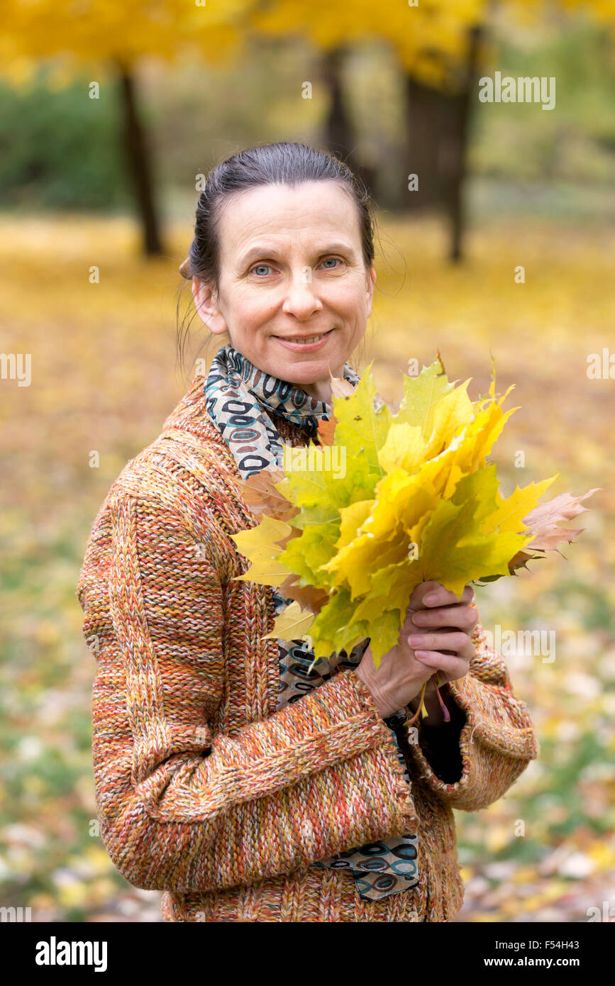 A smiling adult caucasian woman is picking yellow maple leaves in ...