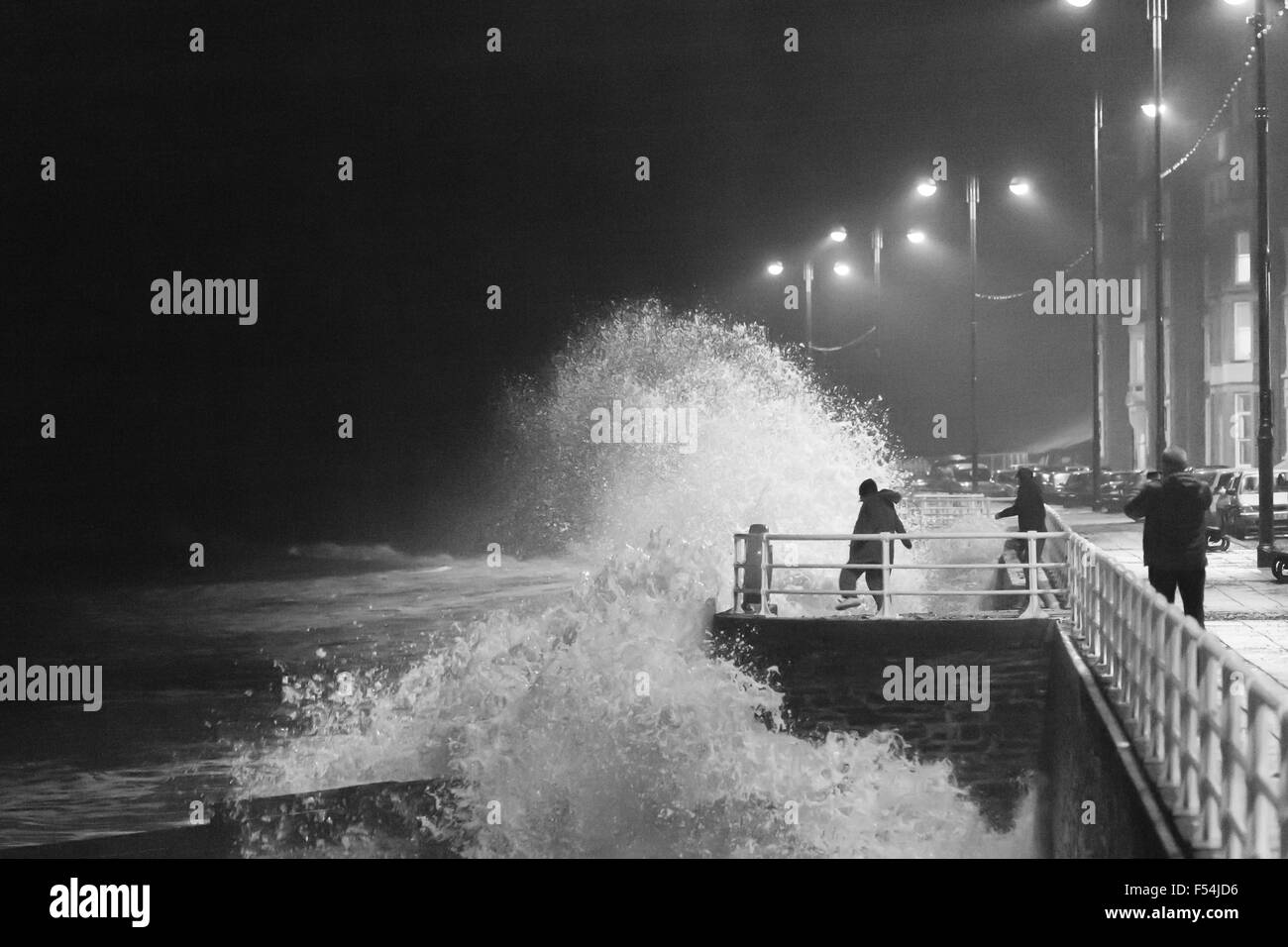 Aberystwyth, Wales, UK. 27th October, 2015. Teenagers take risks as the waves at high tide this evening crash against the promenade in Aberystwyth, while others enjoy the view from a safe distance. Credit:  Ian Jones/Alamy Live News Stock Photo