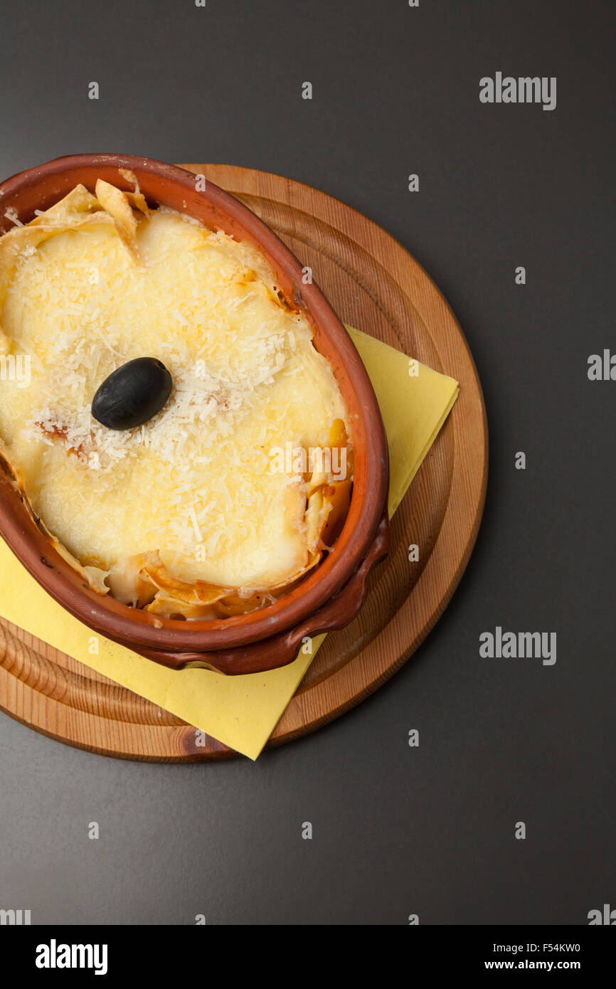 serving of lasagna in a ceramic pot on a wooden base Stock Photo