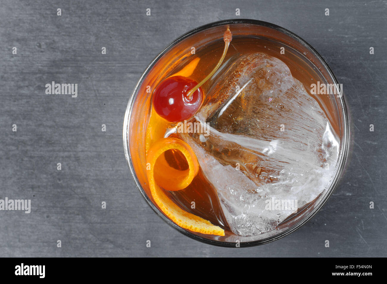 A glass of gin with ice, orange peel and a cherry. Stock Photo