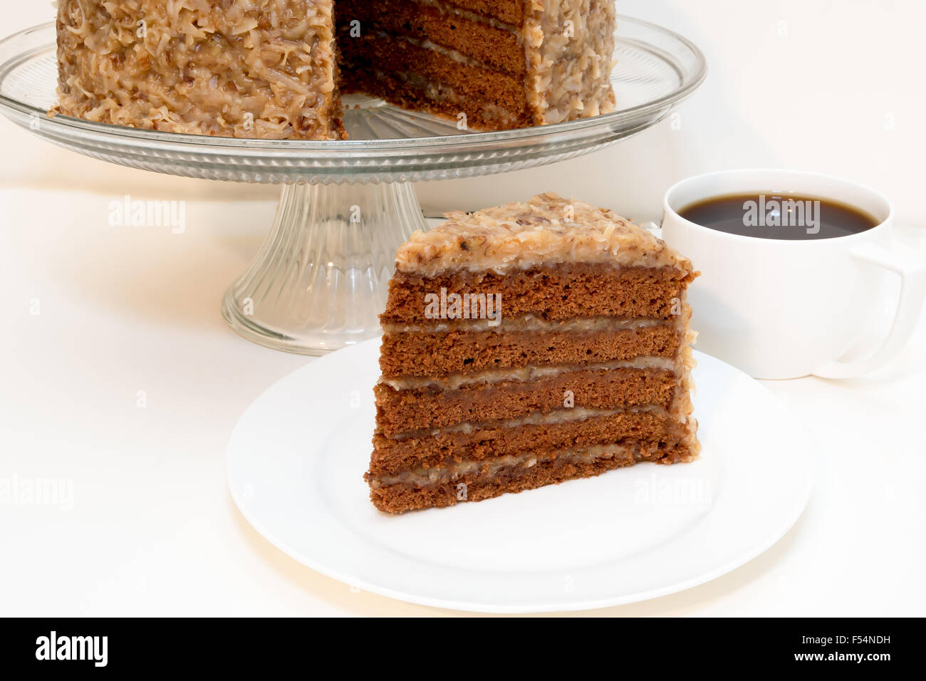Slice of german chocolate cake removed from whole cake  with cup of coffee.  Isolated on white background. Stock Photo