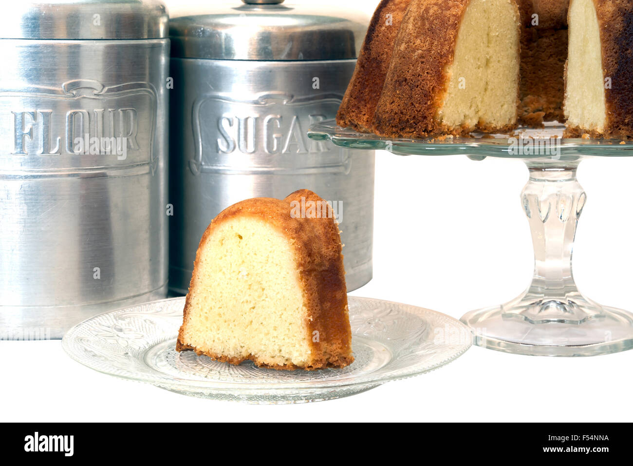 Slice of pound cake removed from whole cake along with flour and sugar canisters.  Isolated on white background. Stock Photo