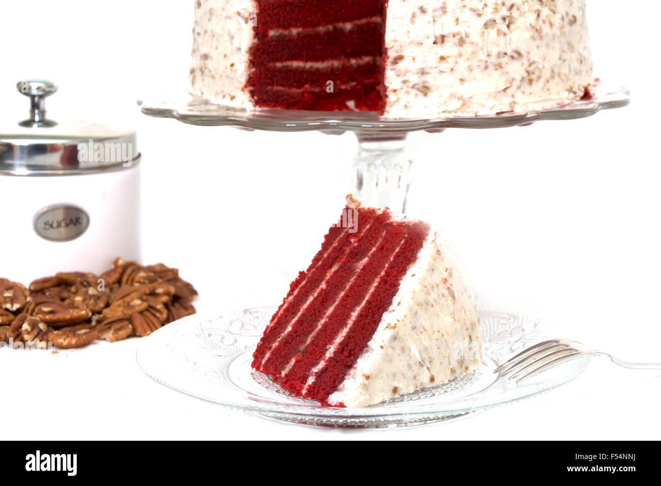 Slice of red velvet cake  along with sliced pecans and sugar canister.  Isolated on white background. Stock Photo
