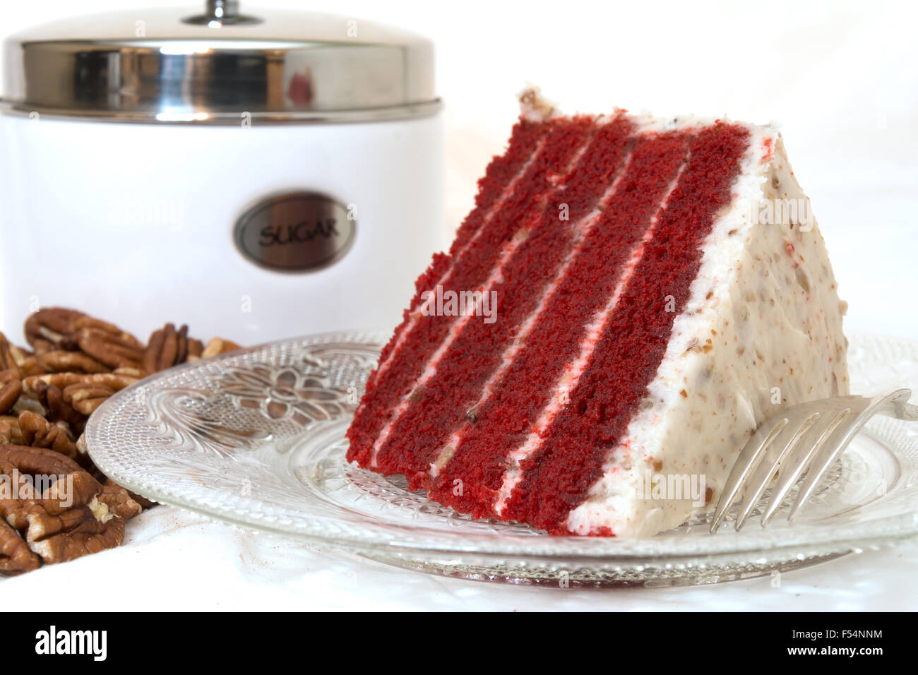 Slice of red velvet cake closeup with sliced pecans and sugar canister in background.   Isolated on white background. Stock Photo