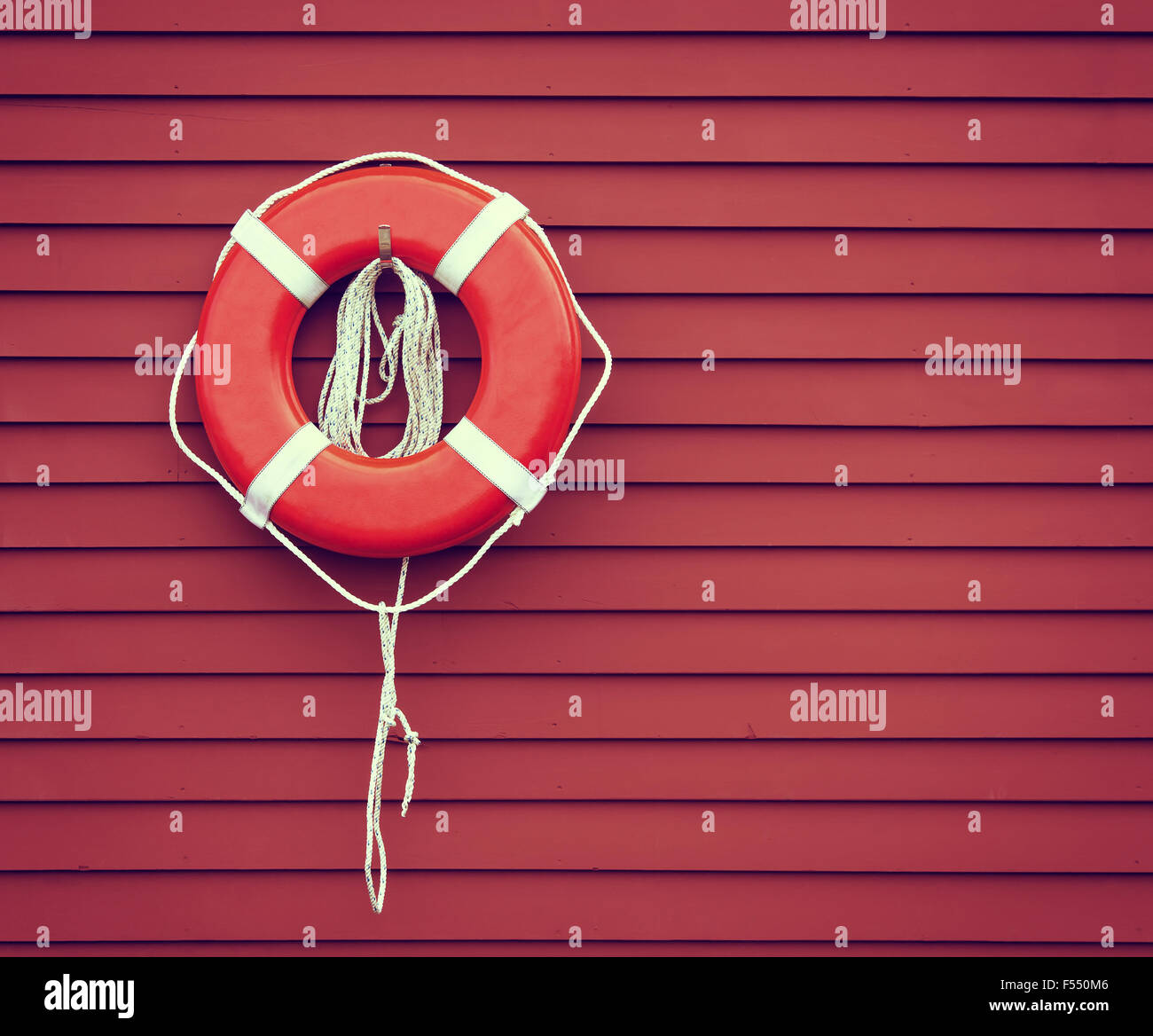 Ring buoy hanging against red, wooden wall background Stock Photo