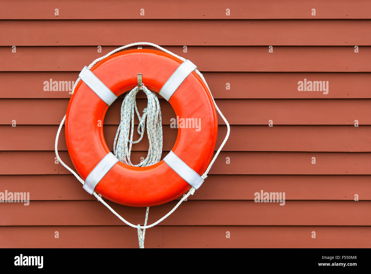 Ring buoy hanging against red wooden wall background Stock Photo