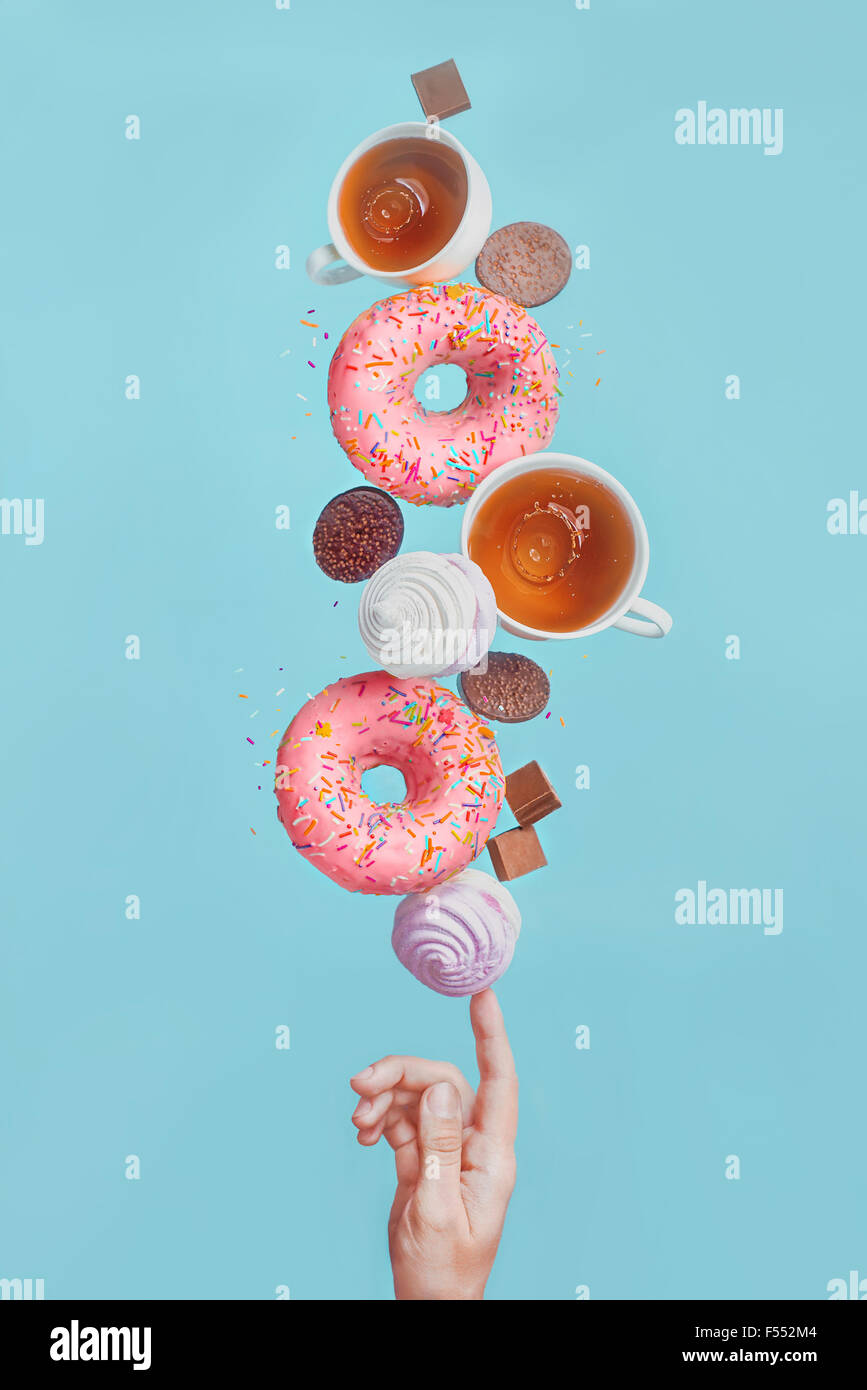 Balancing donuts. Glazed donuts, tea cups, marshmallows and chocolate chips, balancing on the tip of one's finger Stock Photo