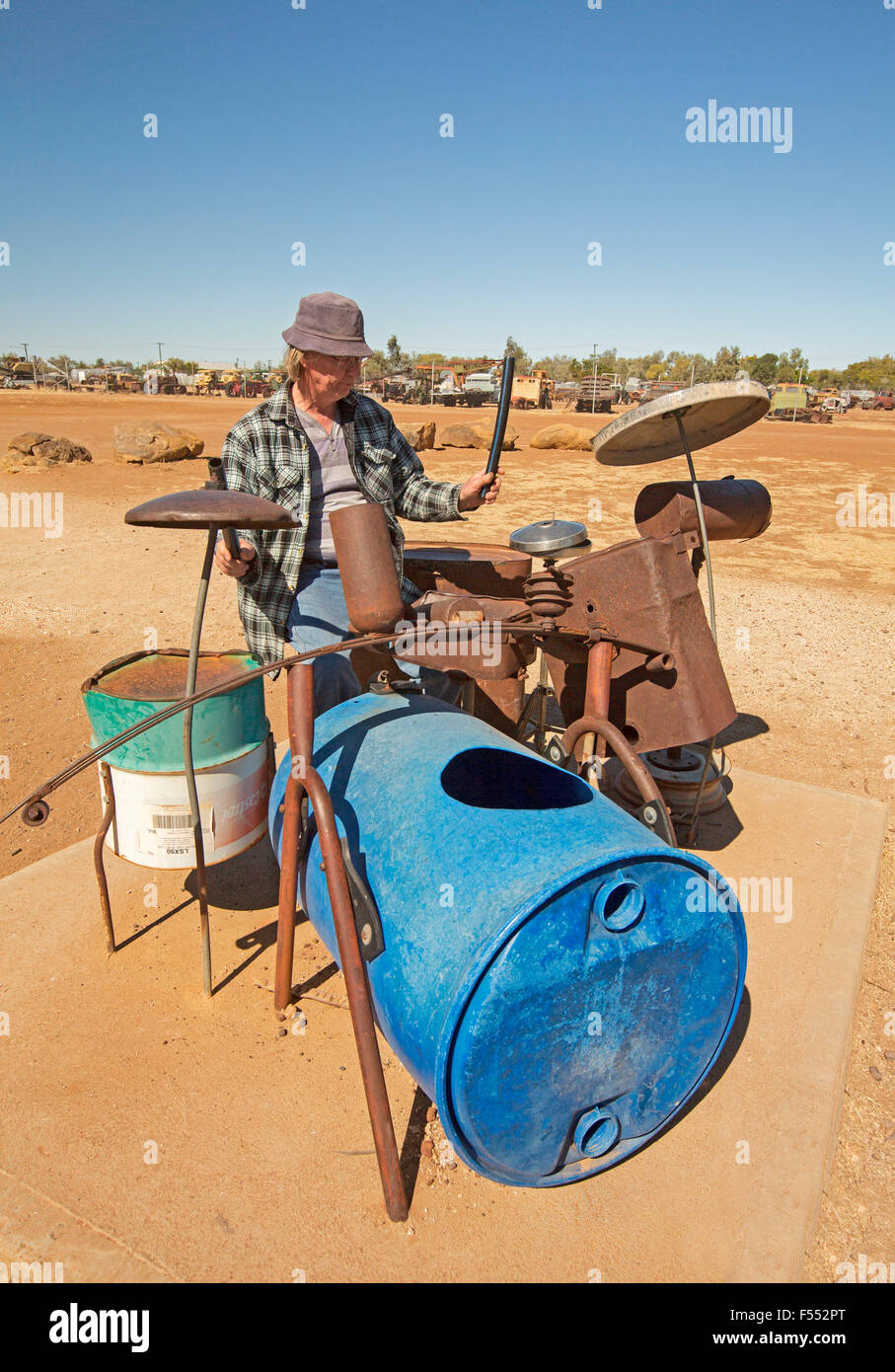 Man playing drum kit made from recycled rubbish at musical fence