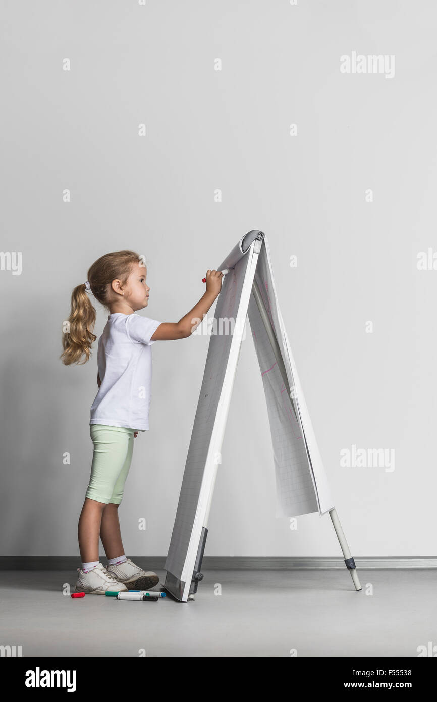 Side view of girl drawing on flipchart against white wall Stock Photo