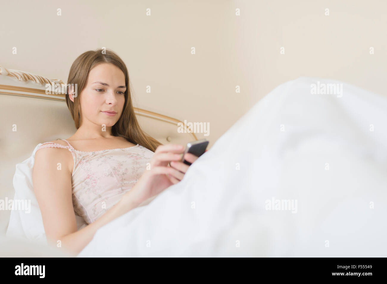 Young woman using smart phone in bed at home Stock Photo