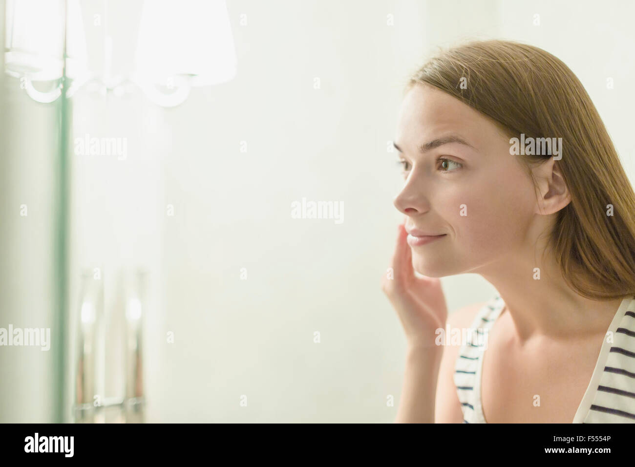 Beautiful woman applying cream on face in domestic bathroom Stock Photo